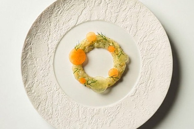 Ring af tartar med urteolie, dill og orange kugler på hvid tallerken
